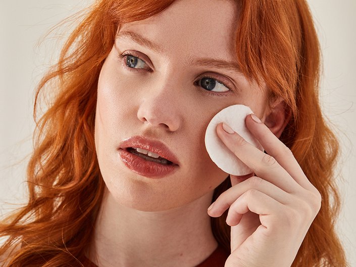 A person with red hair holding up a cotton round to their cheek
